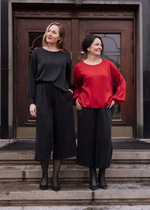 Lataa kuva Galleria-katseluun, Kuvassa kaksi hymyilevää naista, jossa vasemmalla seisovalla päällä musta Rauhassa pusero ja toisella punainen. Puseron malli on klassinen ja ajaton.