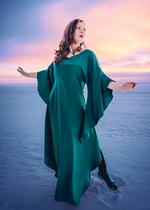 Lataa kuva Galleria-katseluun, Peroonallinen ja näyttävä vihreä satiinimekko. Kuvassa malli seisoo lumessa ja mekon leveät hiat liehuvat tuulessa. Mekko helma edestä melkein maahan asti ja sivuilla taas helma korkeammalla.