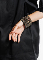 Lataa kuva Galleria-katseluun, mustia ja pronssinvärisiä rannekoruja ranteeessa.
