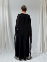 Lataa kuva Galleria-katseluun, Musta sifonkiviitta peittää koko selän, mutta vartalon muodot kuultaa kauniisti sifongin läpi. Viitta ulottuu melkein maahan asti.
