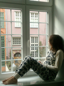 Nainen katselee asunnon ikkunasta ulos unihaalari päällä.